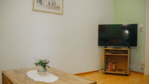 Een woonkamer met een houten tafel, een kleine decoratieve vaas, een boekenkast en een flatscreen televisie op een standaard.