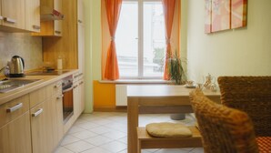 Een keuken met houten kasten, een waterkoker en een raam met oranje gordijnen.
