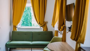 A room with a green sofa, a wooden table, and yellow curtains. - Art Deco Cathedral Apartments by DuHomes (Dubrovnik)