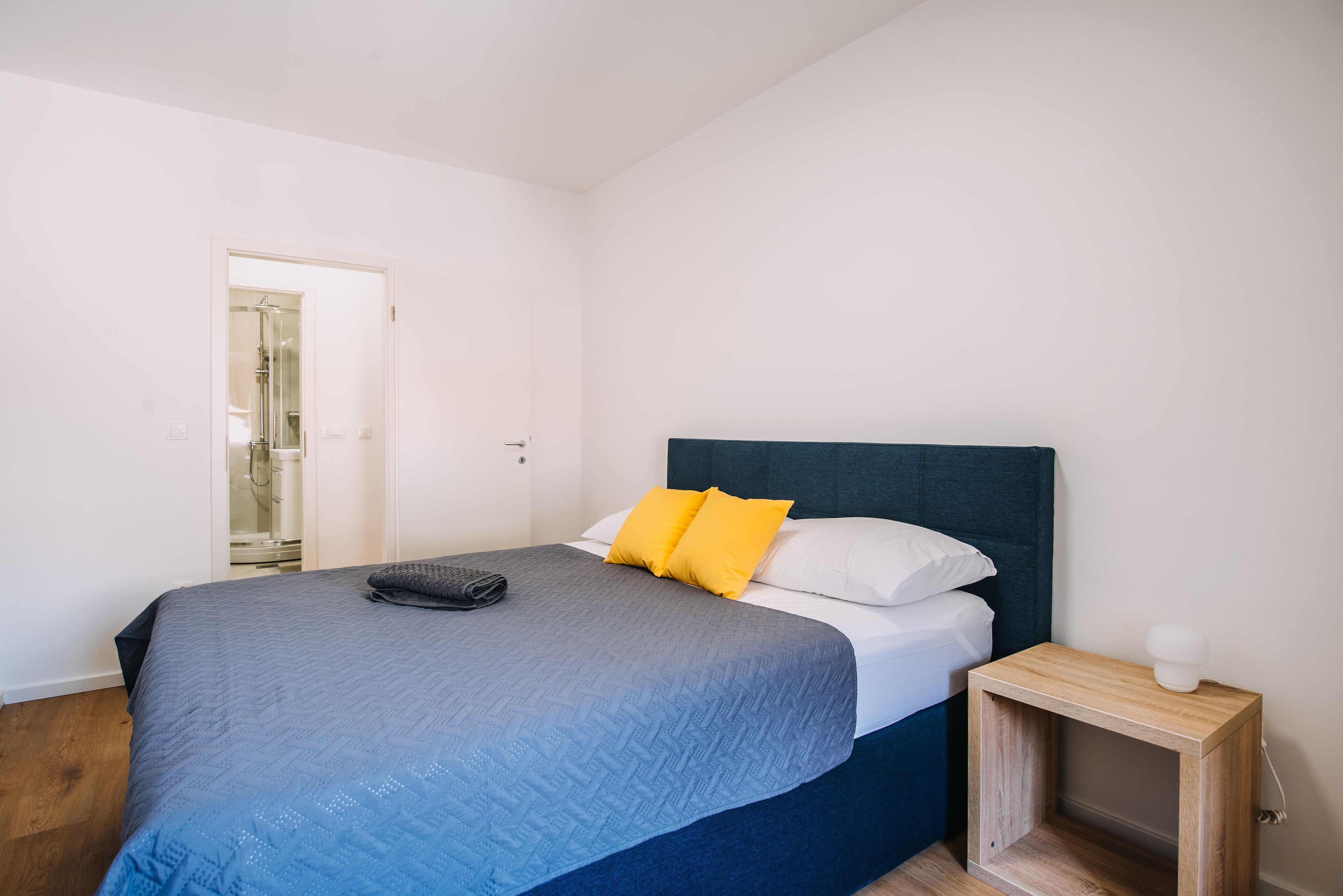 Une chambre à coucher comprenant un lit, une table de chevet et une porte donnant sur une salle de bain.