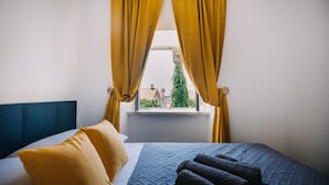 A bedroom with a bed, two pillows, a blanket, and yellow curtains. - Art Deco Cathedral Apartments by DuHomes (Dubrovnik)