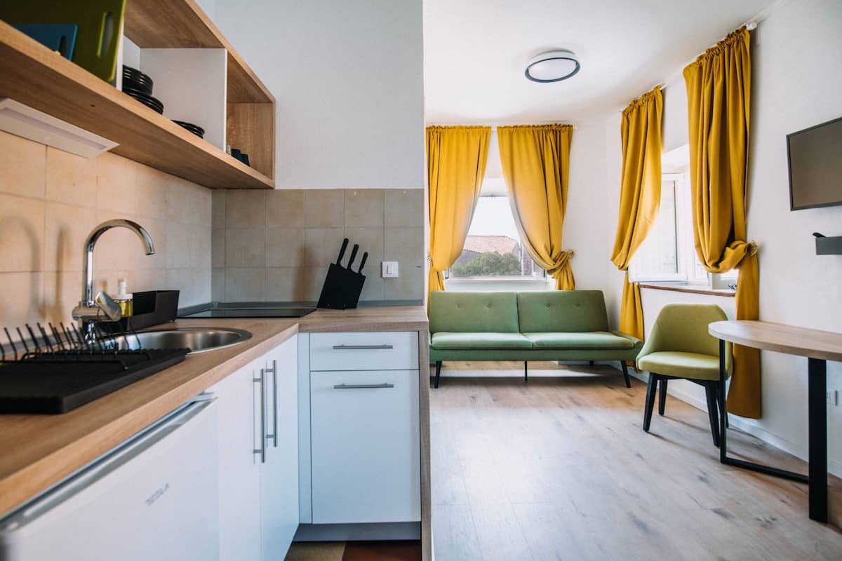 Cocina moderna con un lavamanos, armarios y un sofá verde en una sala de estar luminosa con cortinas amarillas.