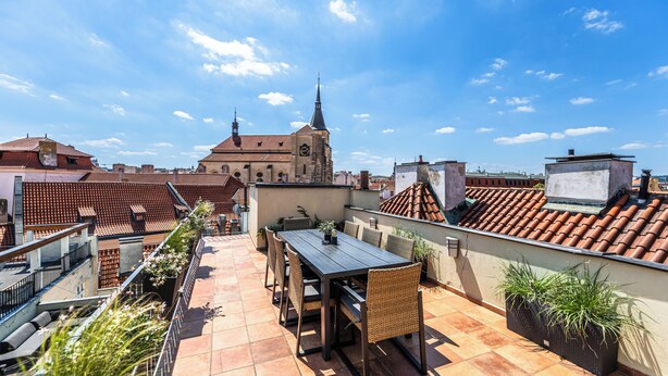 A rooftop terrace with a dining table and chairs, potted plants, and a view of a historic building with a spire. - Charles Apartments in Old Town Prague (Prague)