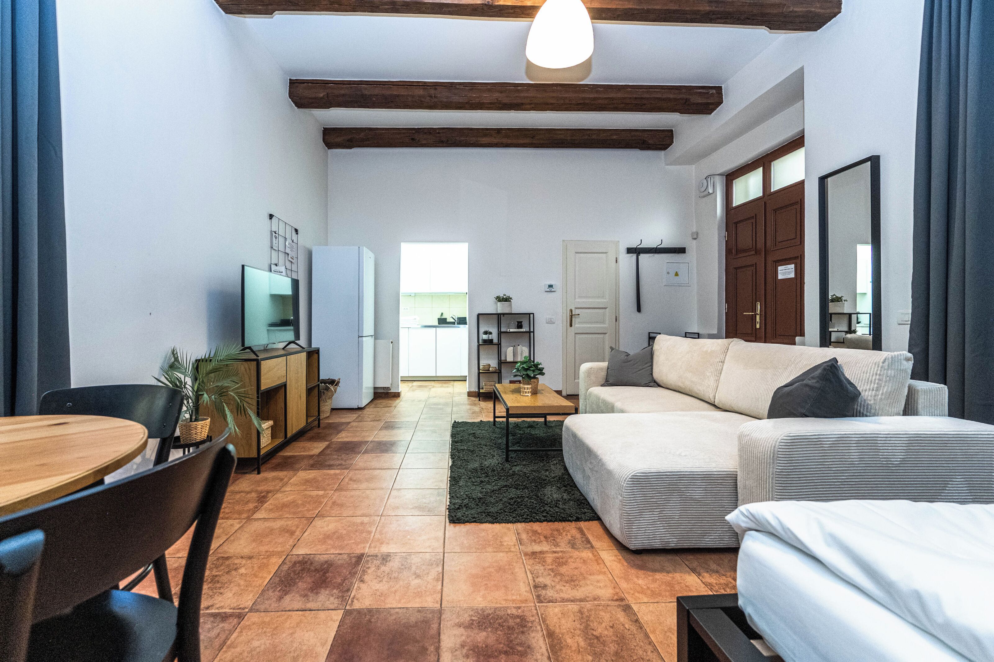 Una sala de estar moderna con un sofá, una mesa de comedor y un televisor. Hay una zona de cocina con armarios y un refrigerador.