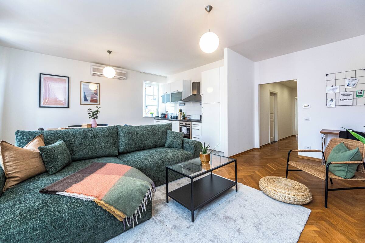 A modern living room with a green sectional sofa, a glass coffee table, and a wicker chair.