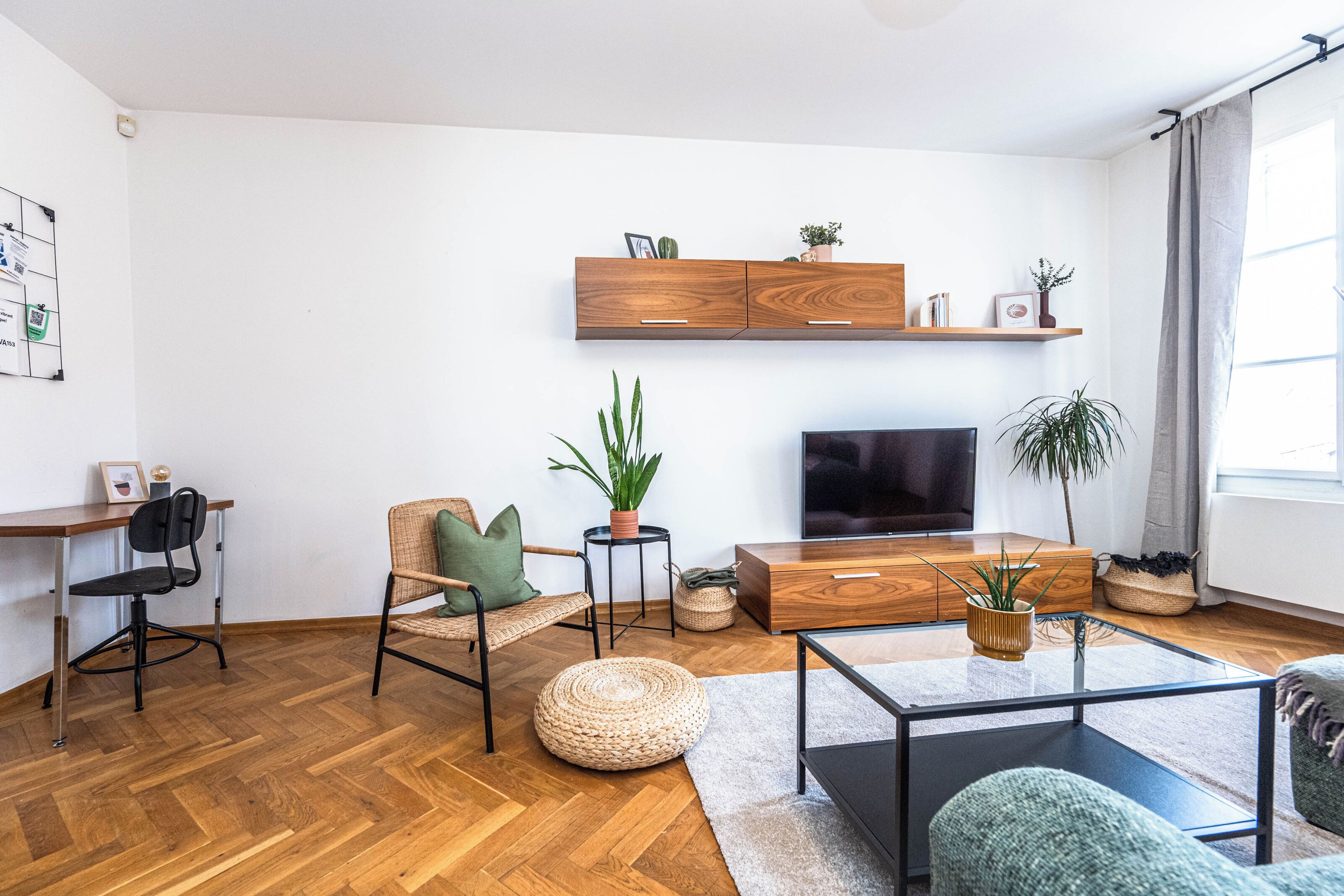 Un salon moderne doté d’un parquet en bois à motifs en chevrons, d’un téléviseur à écran plat, d’une table basse en bois et d’un coin salon confortable avec un fauteuil et un pouf.