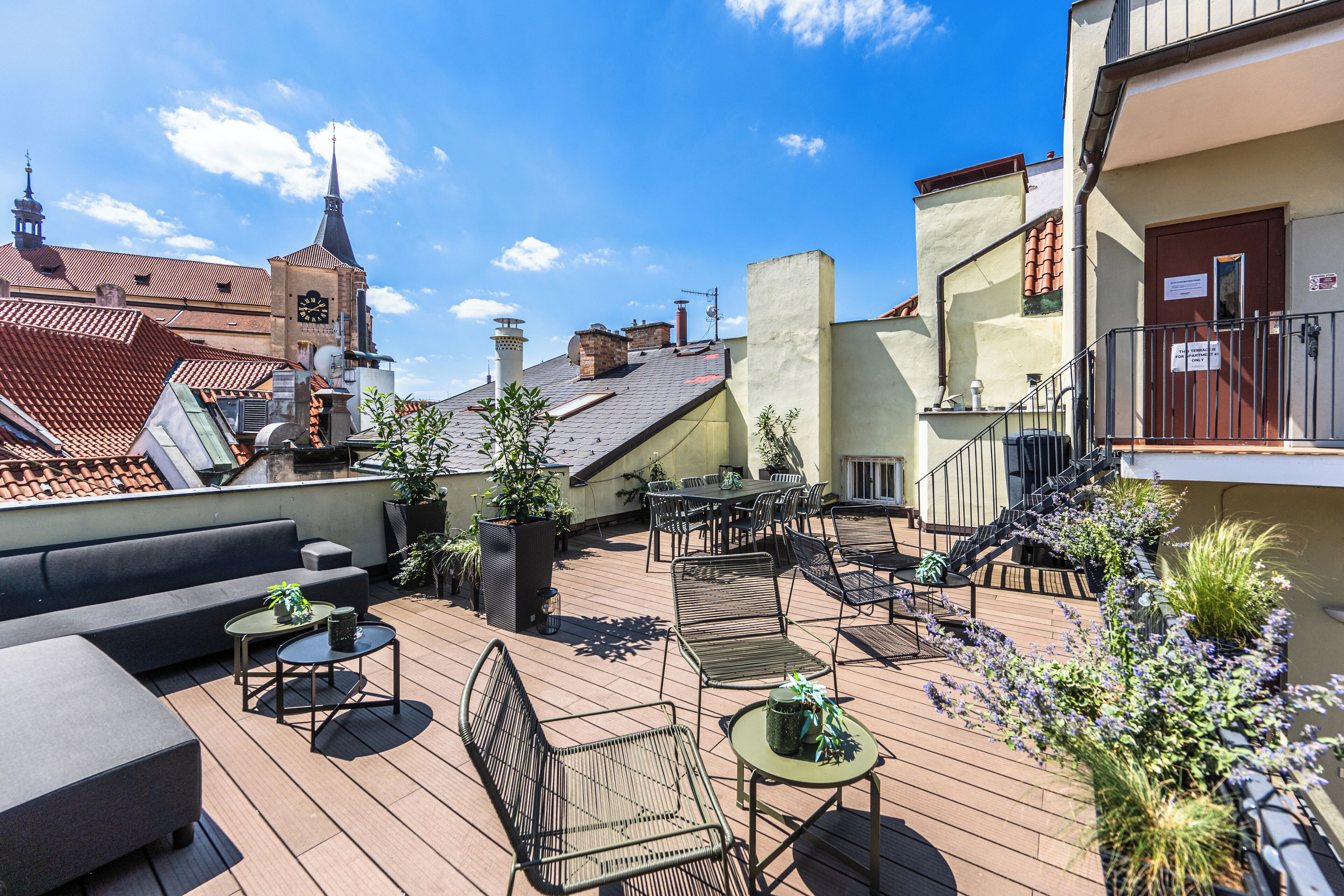 A rooftop patio with outdoor seating, a clock tower in the background, and a staircase leading to an upper level.