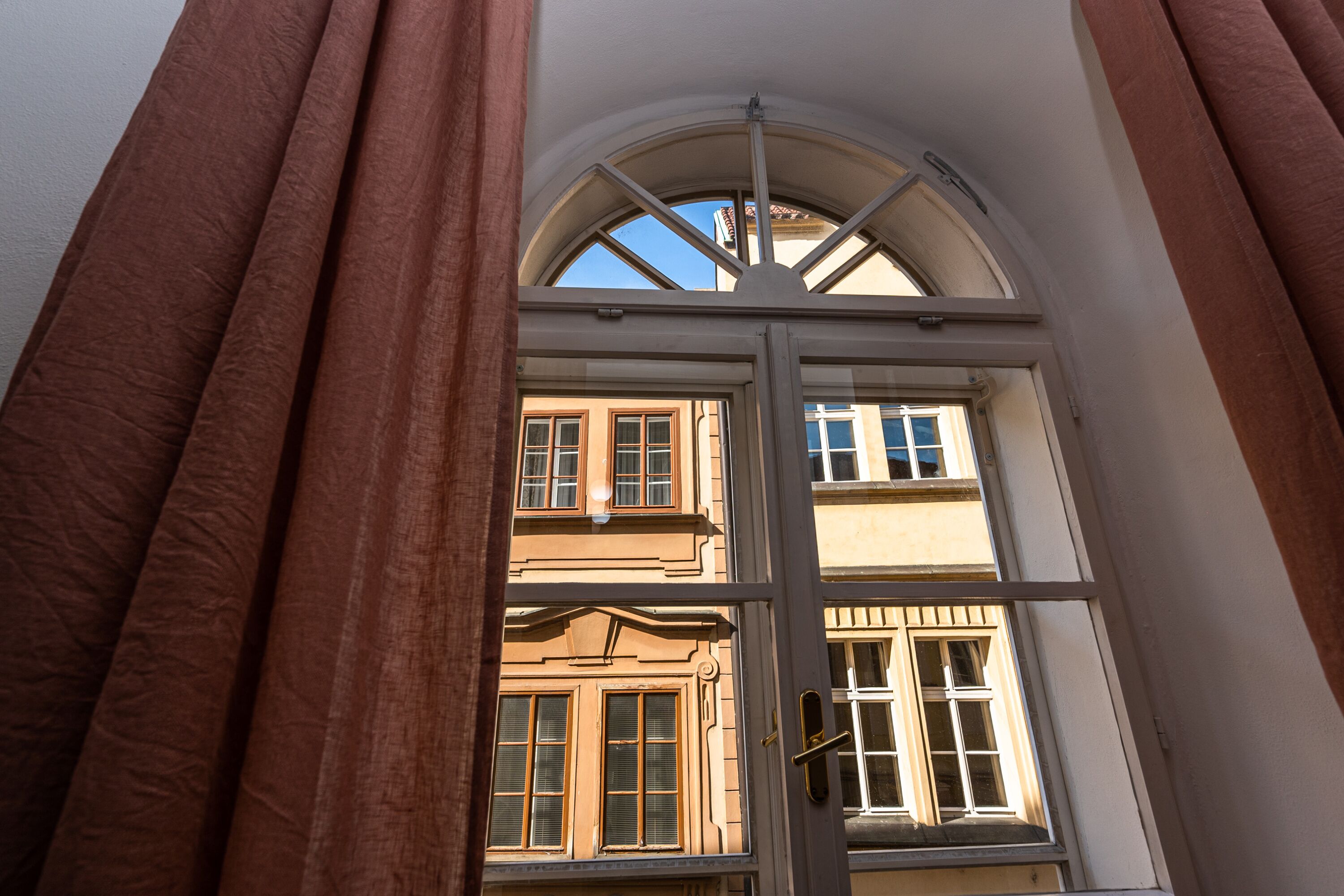 A view through a window with a white frame and a door, revealing a building with multiple windows and a classic architectural style.