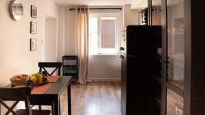 Cocina compacta con una mesa de comedor para dos personas, un refrigerador y una ventana con cortinas.