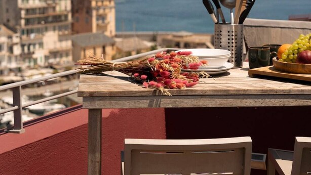 A balcony with a table set for dining, overlooking a cityscape and the sea. - Apartment Roof Top with spa (Bastia)