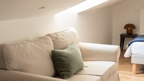 Una sala de estar moderna y minimalista con un sofá beige, un cojín verde y una mesita de noche con una lámpara.