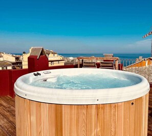 A wooden hot tub on a deck with a view of the ocean and buildings in the background. - Apartment Roof Top with spa (Bastia)