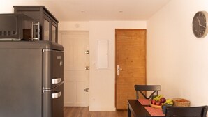 A compact kitchen with a refrigerator, a microwave, and a wooden door. A dining table with chairs and a fruit basket are visible. - Apartment Roof Top with spa (Bastia)