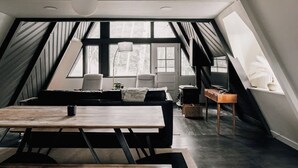 A loft-style room with a dining area, seating, and a large window. - Modern A-Frame | Mountain Views | Evergreen (Evergreen)