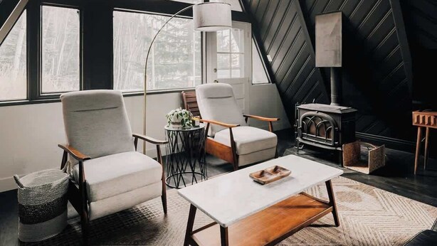 A modern loft with a sloped ceiling, large windows, a fireplace, and contemporary furniture. - Modern A-Frame | Mountain Views | Evergreen (Evergreen)