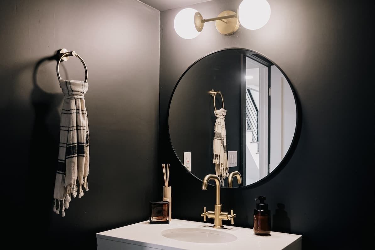 A bathroom with a round mirror, a towel rack, a sink, and a wall-mounted light fixture.