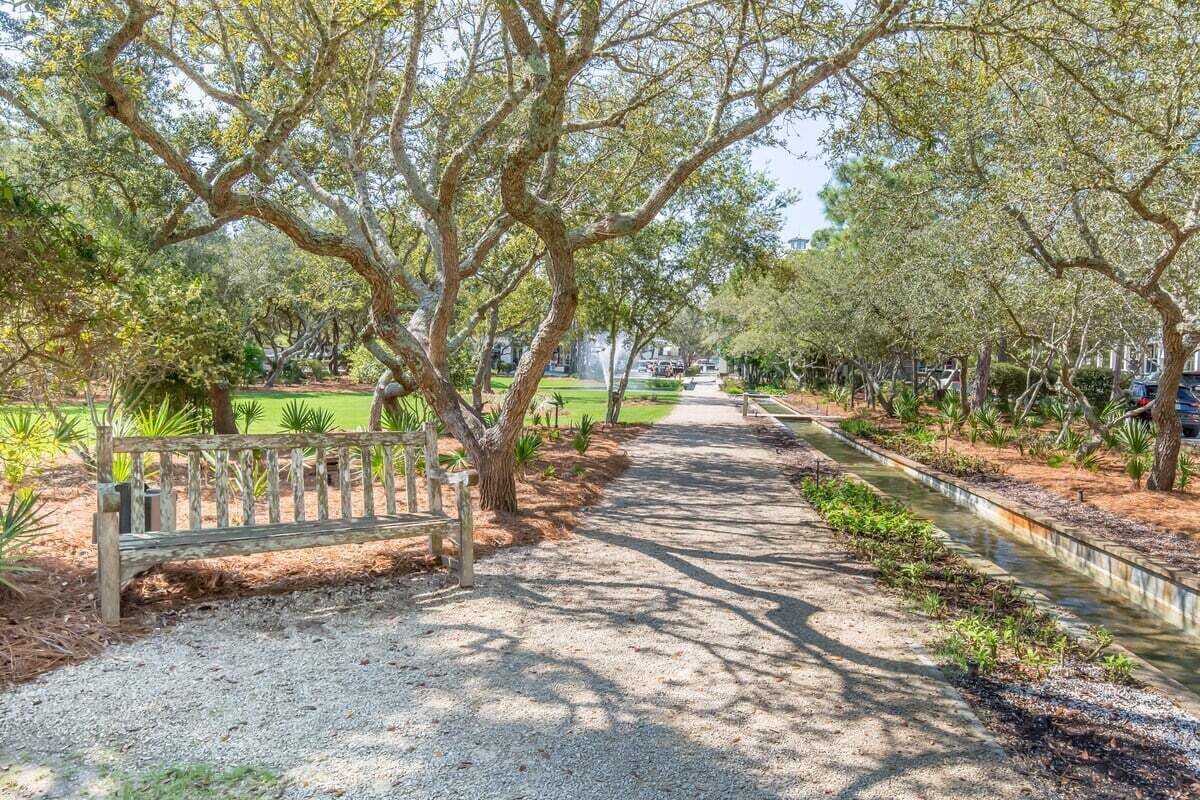 A pathway lined with trees and a bench, leading to a building in the distance.
