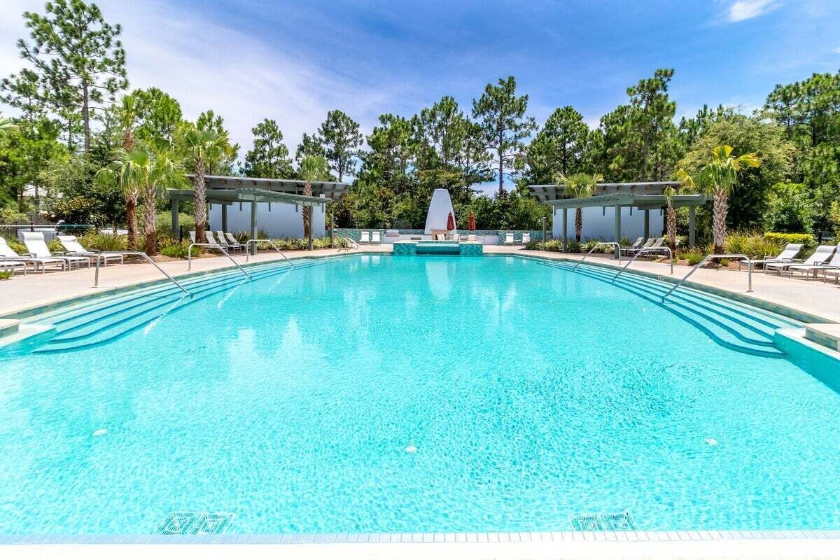 A clear blue swimming pool with lounge chairs and a covered seating area, surrounded by trees.