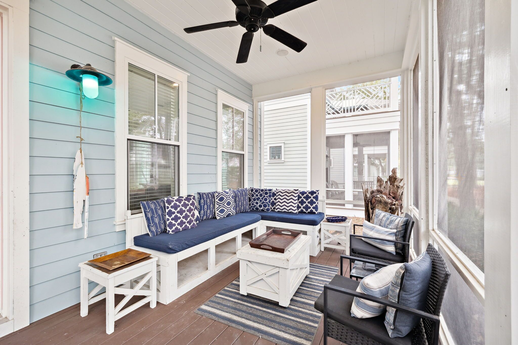 A covered porch with a blue and white sectional sofa, white furniture, and a ceiling fan.