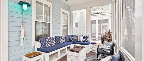 A covered porch with a blue and white sectional sofa, white furniture, and a ceiling fan.