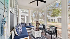 A covered porch with a blue sofa, a wooden coffee table, and a chair.
