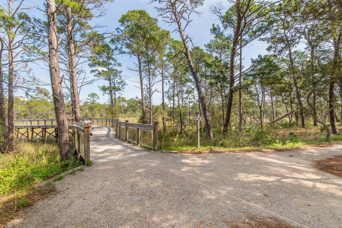 A gravel path leading through a forested area with a wooden bridge and a signpost.