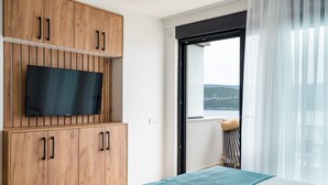 A bedroom with a bed, a TV mounted on wooden cabinets, a balcony with a view of the landscape, and sheer curtains. - 3 Studio apartment with Sea View (Neum)