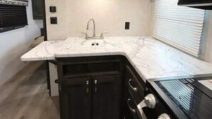 A compact kitchen with a marble countertop, a built-in sink, and a black stove.