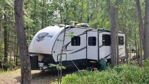 A white RV with a black stripe parked in a wooded area.