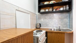 Una cocina compacta con encimera de madera, estufa integrada, pileta y estante con vajilla y utensilios.