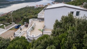 Zona residencial con vista a un lago y montañas. Se observa un edificio blanco con balcón y un área pavimentada con mobiliario exterior.