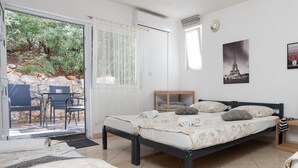 Ein Schlafzimmer mit Bett, kleinem Tisch und Stuhl. Ein Fenster mit Vorhängen, ein Bild vom Eiffelturm und Blick auf Bäume und Felsen vor dem Fenster.
