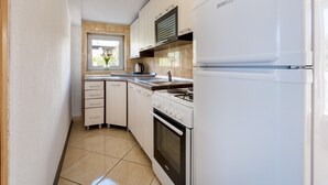 Een kleine keuken met een witte koelkast, fornuis en oven. Er is een raam met uitzicht op groen.