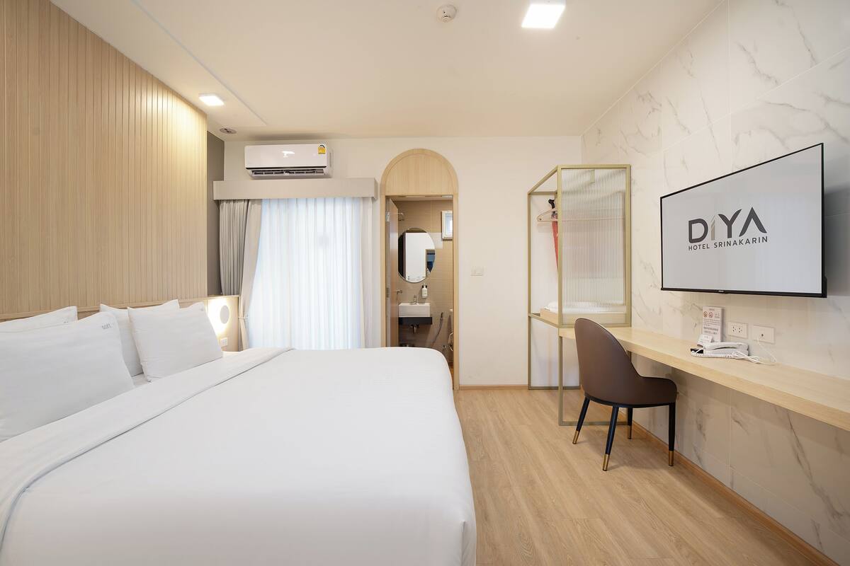 A hotel room with a bed, a desk, a chair, a TV, and a bathroom visible through an archway.