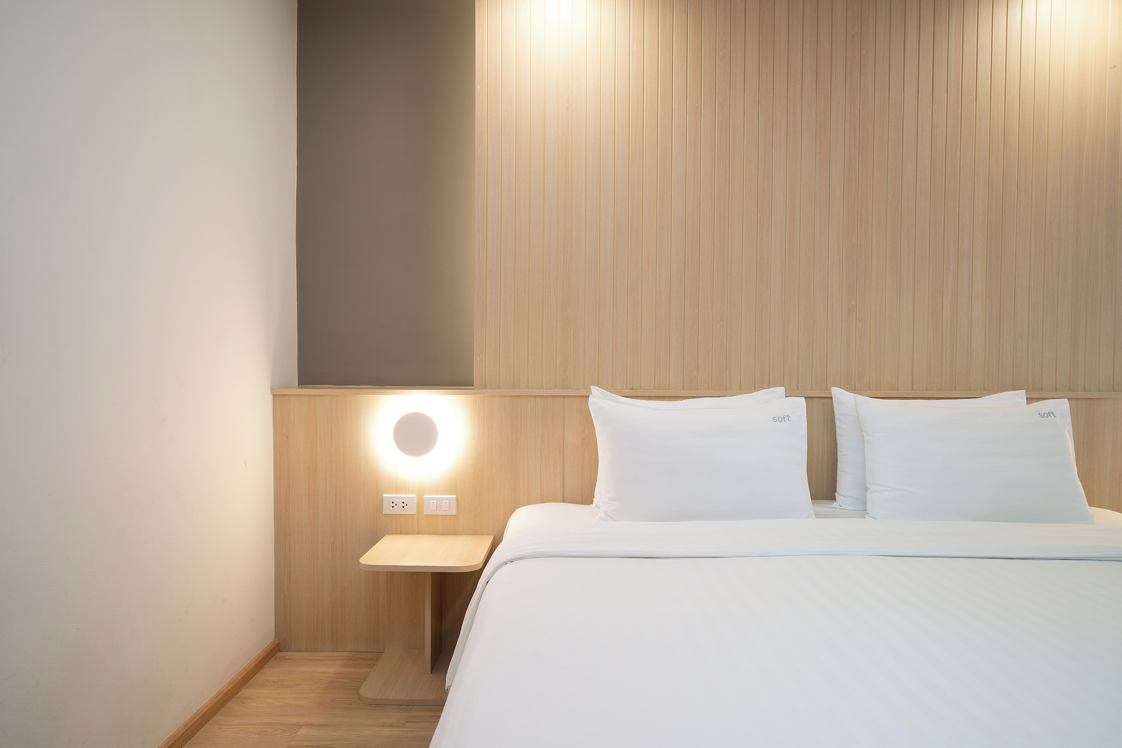 Une chambre d’hôtel avec une tête de lit en bois, une table de chevet dotée d’une lampe ronde et deux oreillers blancs portant l’inscription « sort ».