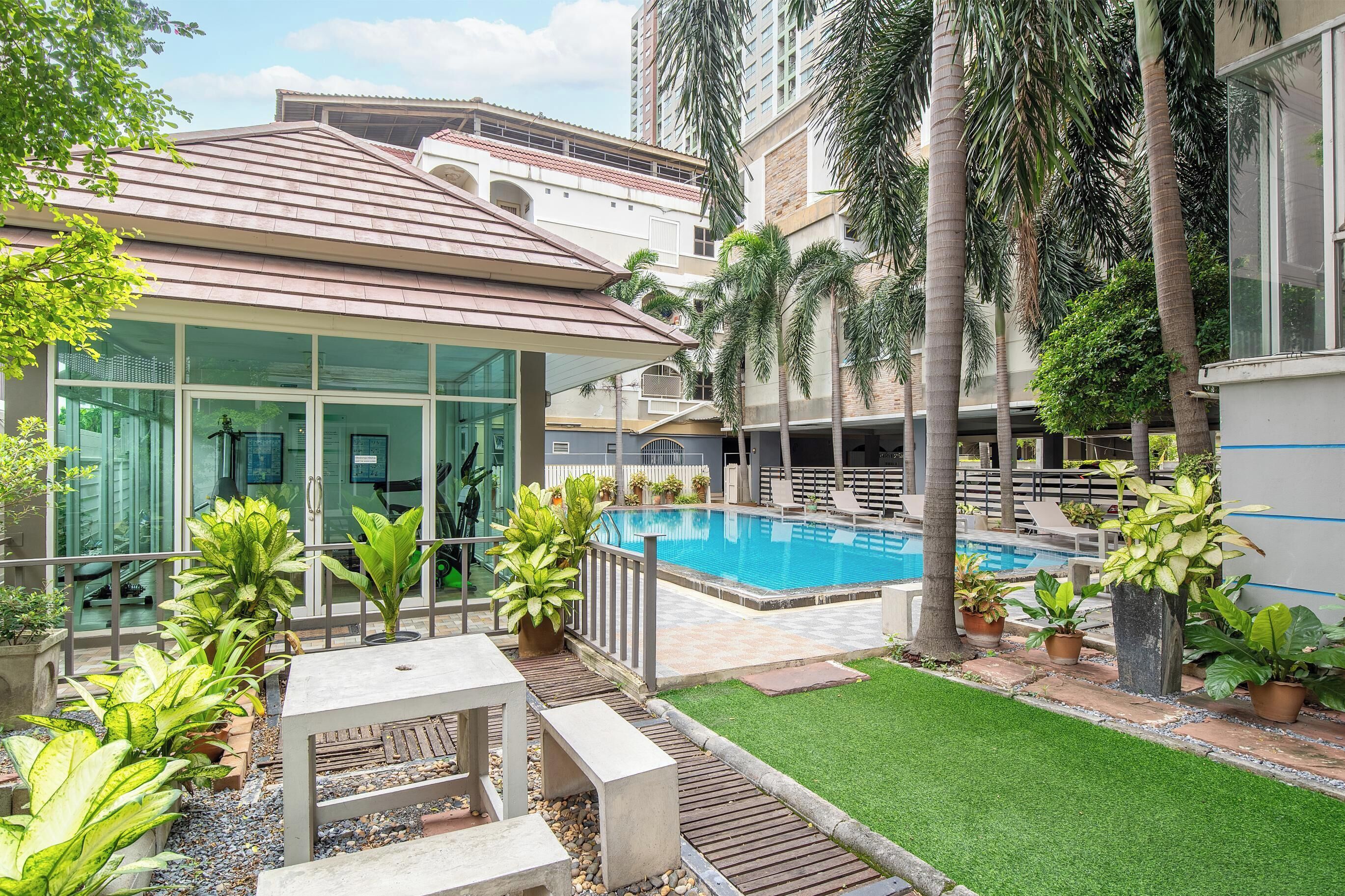 A modern building with a swimming pool, surrounded by palm trees and potted plants.