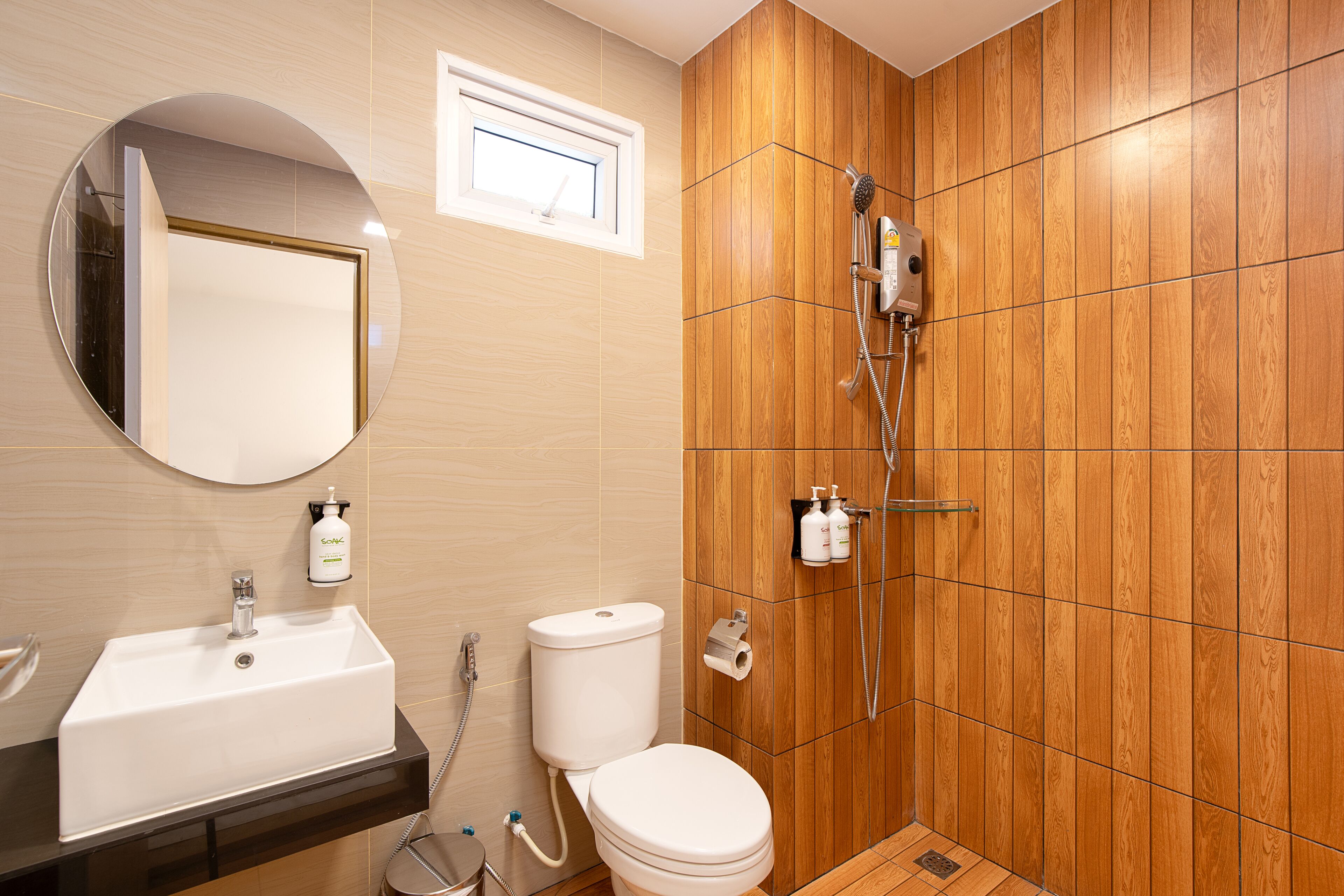 A bathroom with a wooden panel wall, a white sink, a toilet, a shower with a handheld showerhead, and a mirror with a round frame.