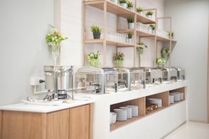 A buffet setup with food dispensers, a coffee machine, and a counter with stacked plates.