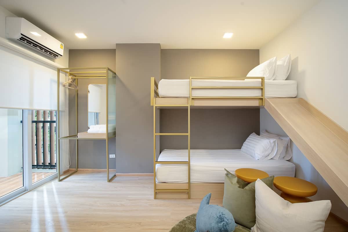 A modern, compact room with bunk beds, a glass wardrobe, and a small seating area with cushions.