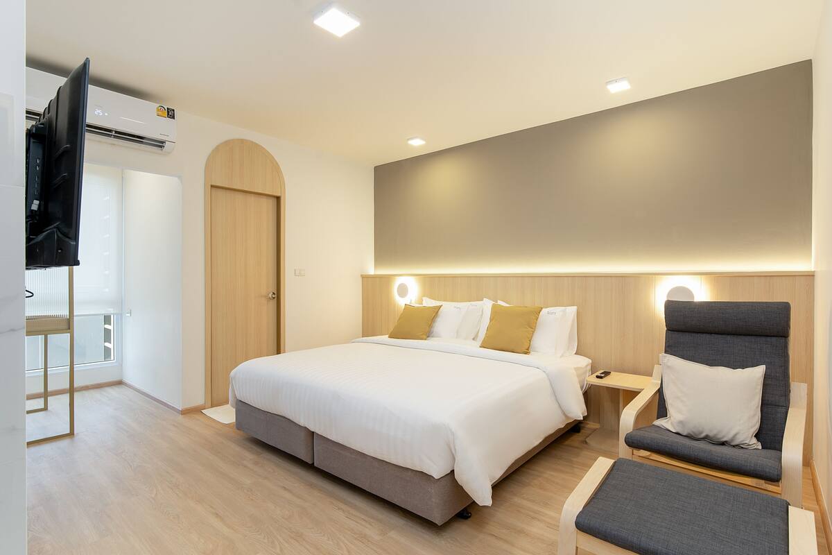 A modern hotel room with a large bed, a seating area, and a flat-screen TV.