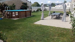 Een achtertuin met een zwembad, een overdekt terras en een tafel met stoelen.
