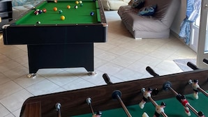 Een biljart tafel in een kamer met een houten plafond, een bank en een stoel.