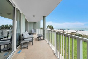 En balkon med udsigt over stranden, en sofa, et bord og en stol.