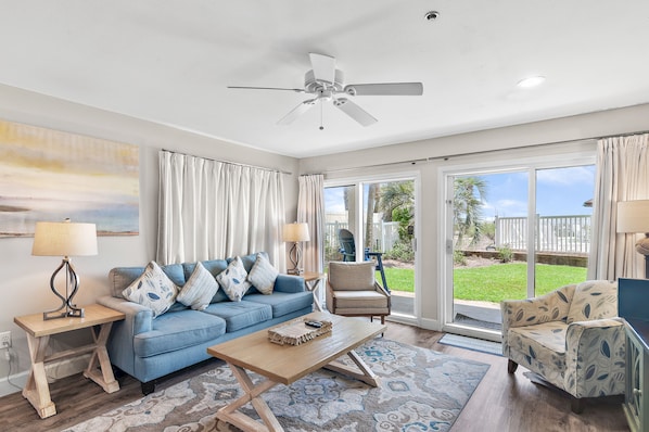A living room with a blue sofa, a wooden coffee table, a chair, and a ceiling fan. - Beach Service Included! | Beachfront | Steps to Gulf Pool | Windancer 101 (Miramar Beach)