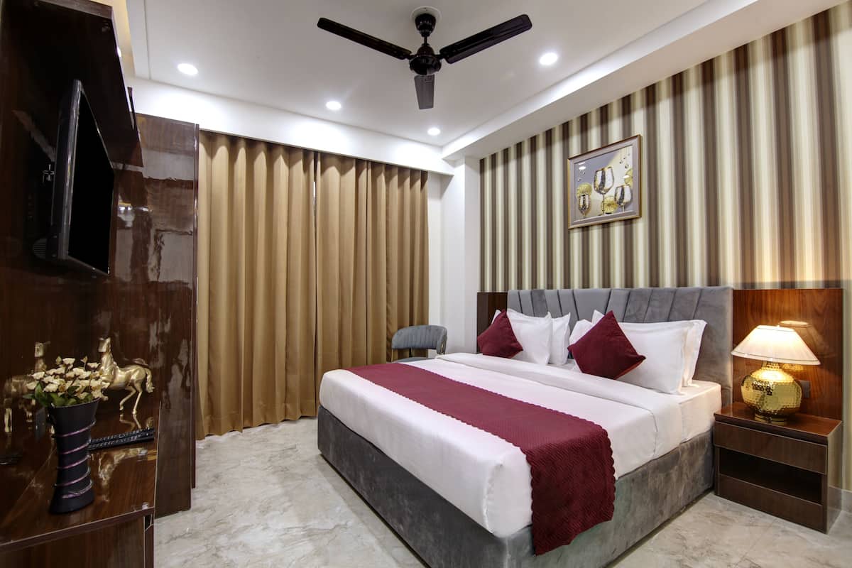 A hotel room with a large bed, a ceiling fan, a TV, and a nightstand with a lamp.