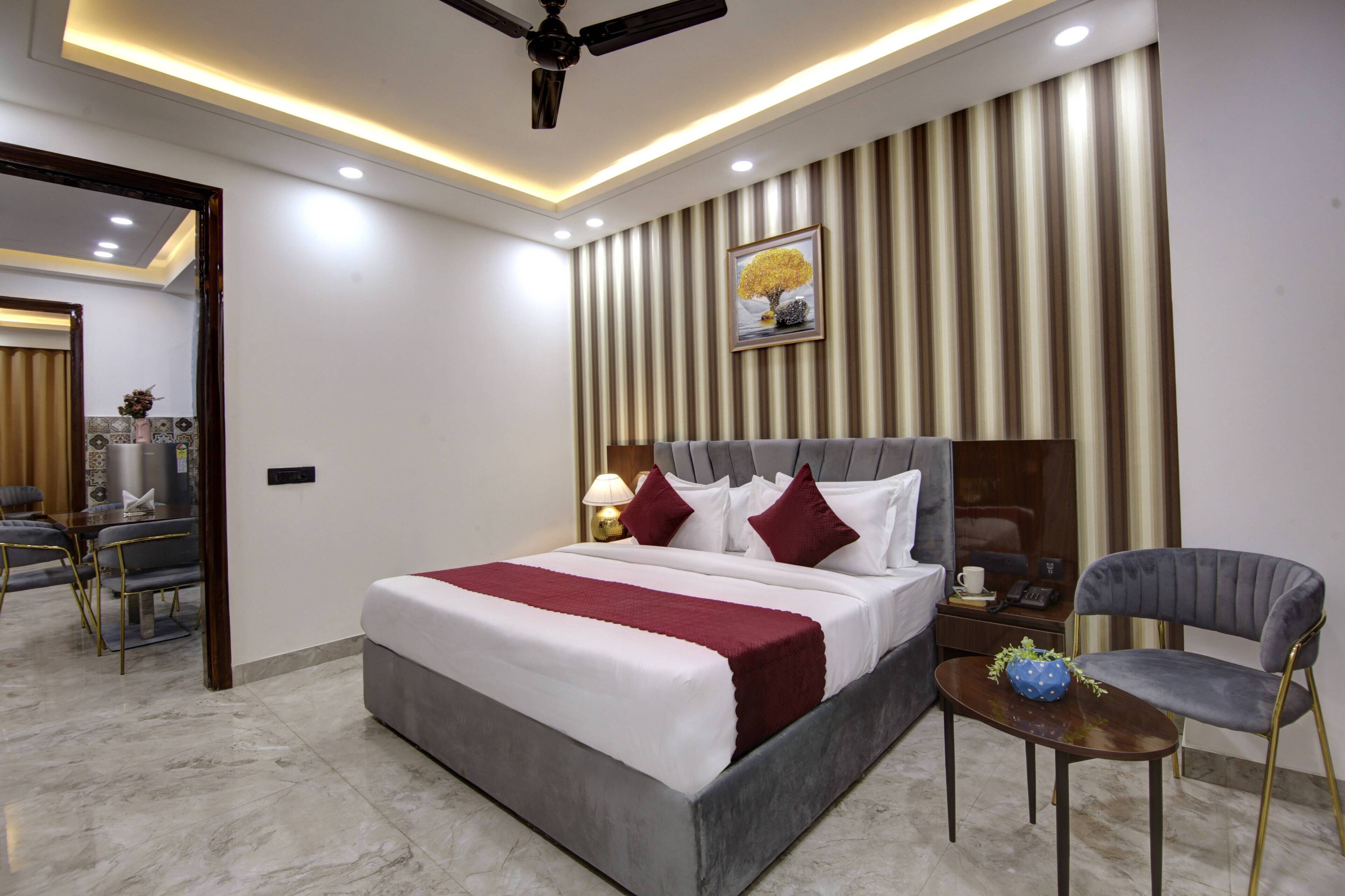 A modern hotel room with a large bed, a desk, a chair, a ceiling fan, and a wall-mounted picture.