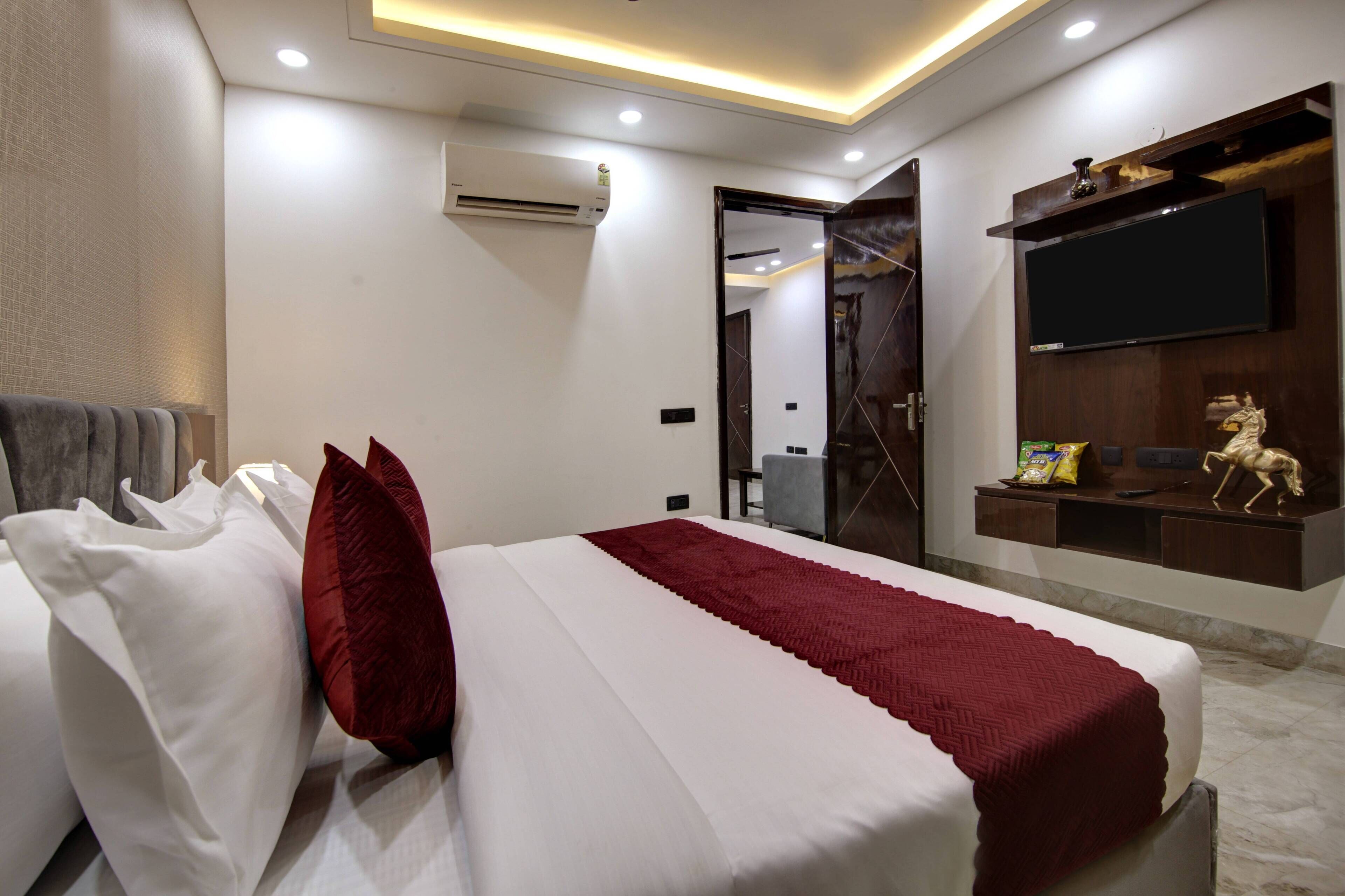 A modern hotel room with a neatly made bed, a flat-screen TV mounted on the wall, and a small statue on the dresser.