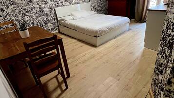 A small, compact room with a bed, a wooden table with chairs, and a small desk.