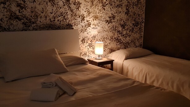 A hotel room with two beds, a nightstand with a lamp, and a floral wallpaper.