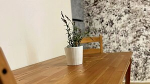 A wooden dining table with chairs, a white pot with a plant, and a patterned wall in the background.